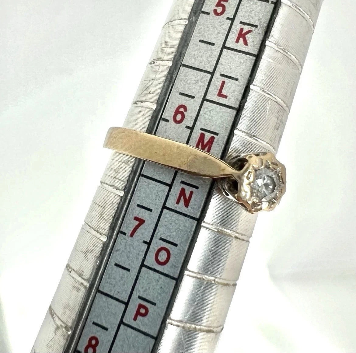 Gold ring with a diamond on a metal ring sizer for size measurement.