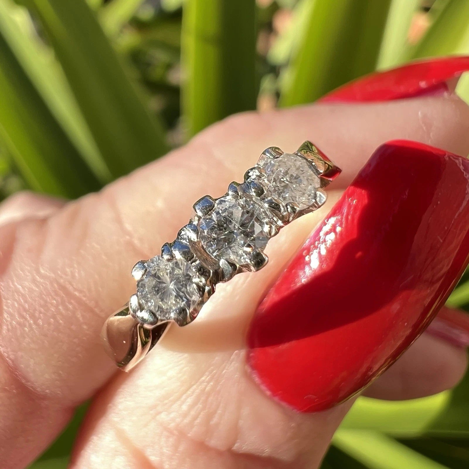 Diamond ring being held by finger with red nail polish against a blurred green background