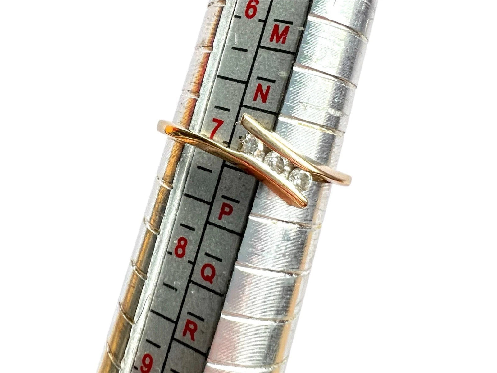 Close-up of a metallic ring sizer with measurement scale and gold ring on a white background