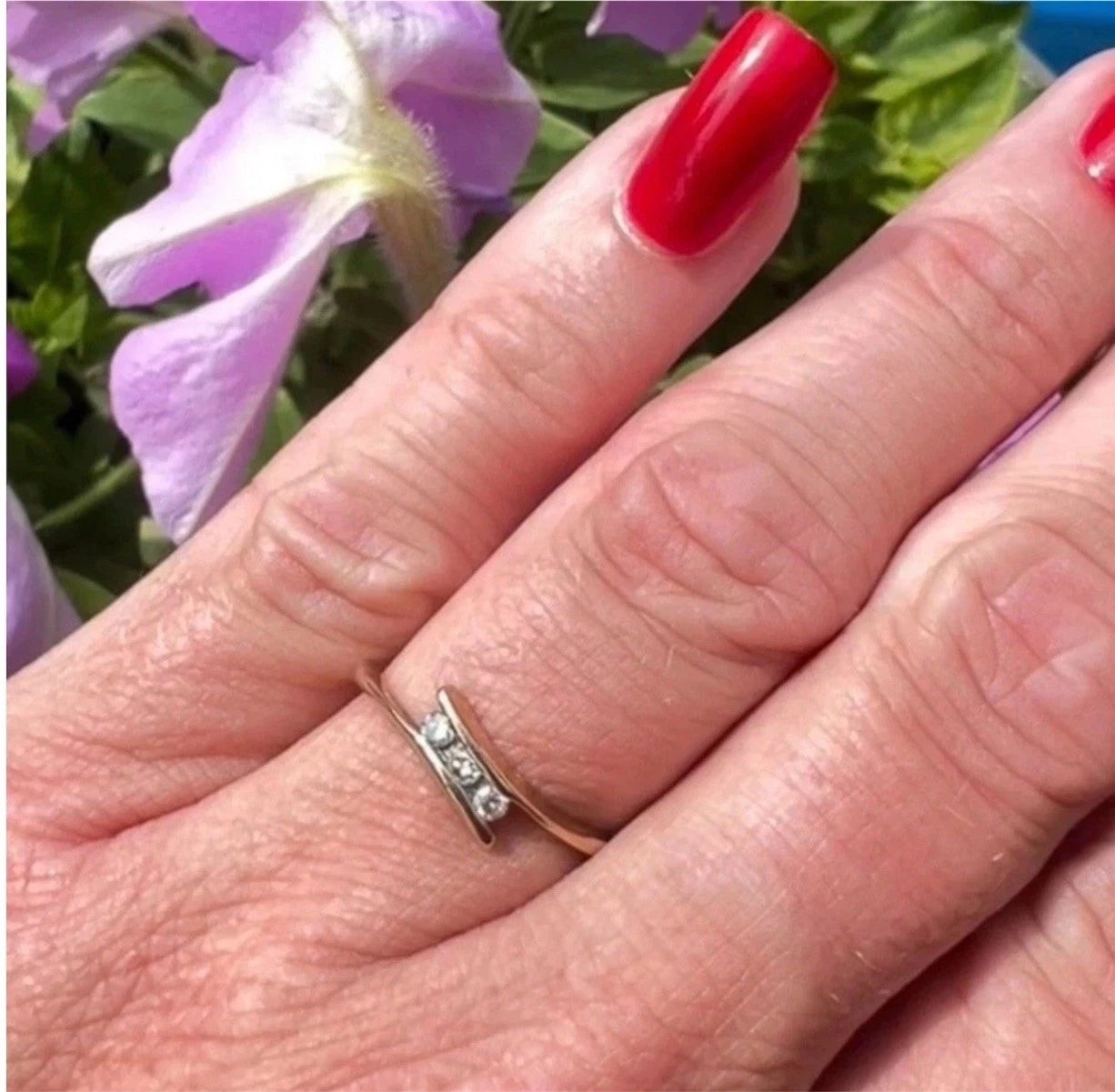 Hand with a gold diamond three stone ring on a blurred floral background