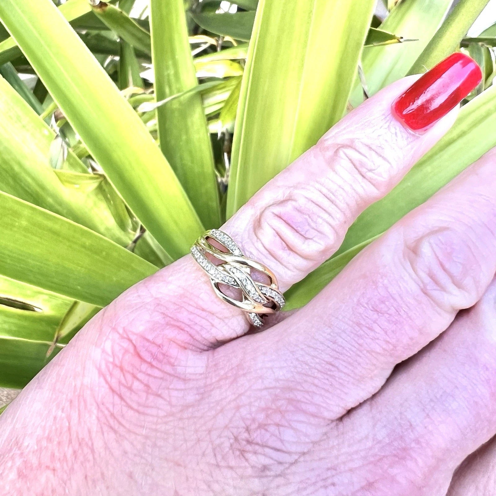 Hand wearing a gold ring with green leaves in the background
