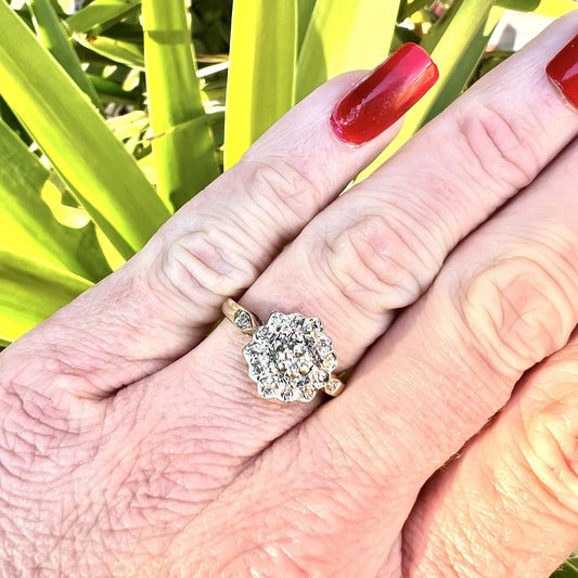 Hand wearing a diamond cluster ring with a blurred green background