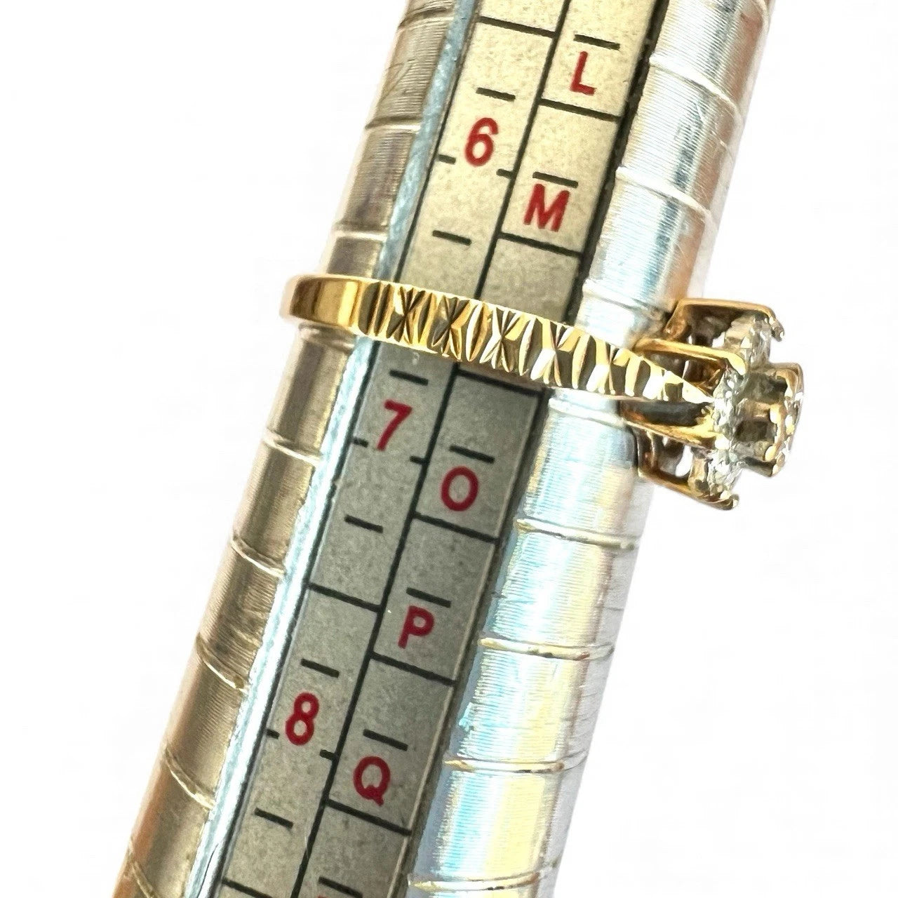 Gold ring with diamond on a ring sizer against a white background