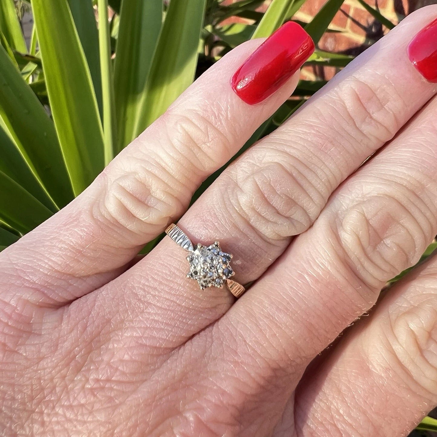 Close-up of a hand wearing a diamond ring with a blurred green background