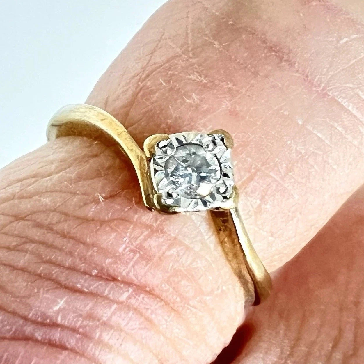 Gold ring with a diamond on a finger against a light background