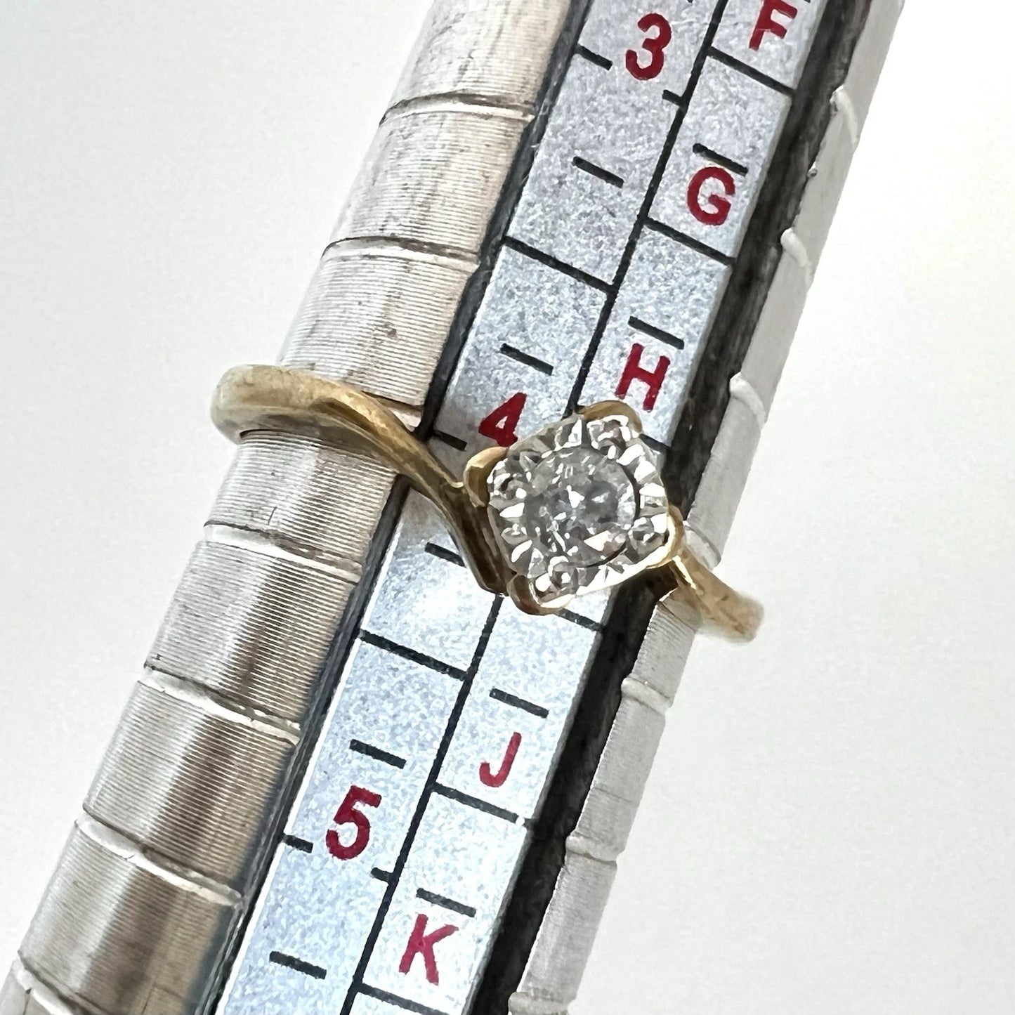 Gold ring with diamond on a ring sizer for size reference
