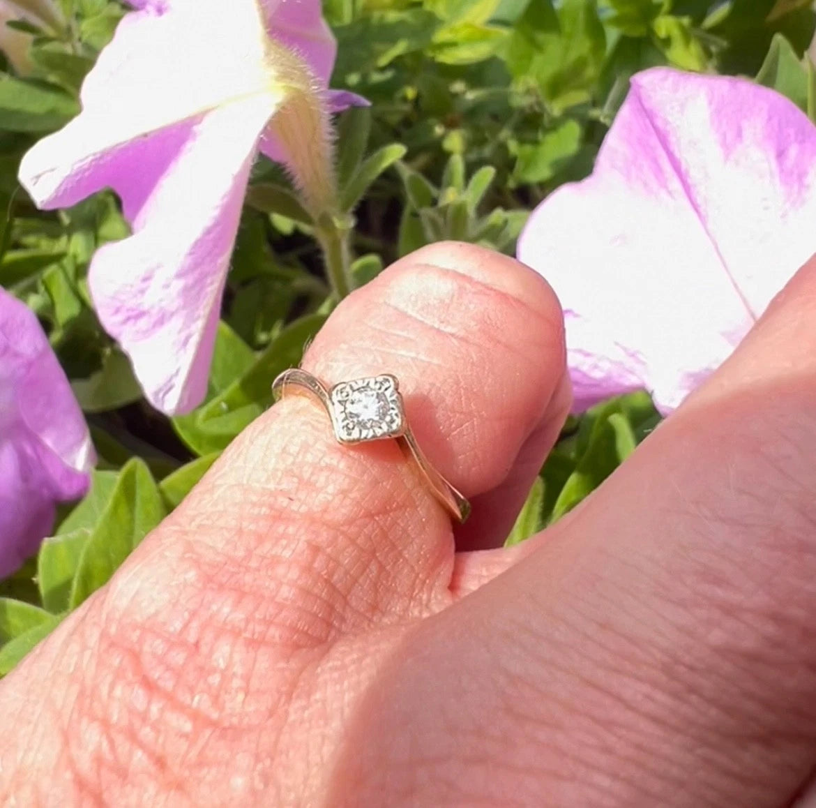 Hand wearing a diamond ring with pink flowers in the background