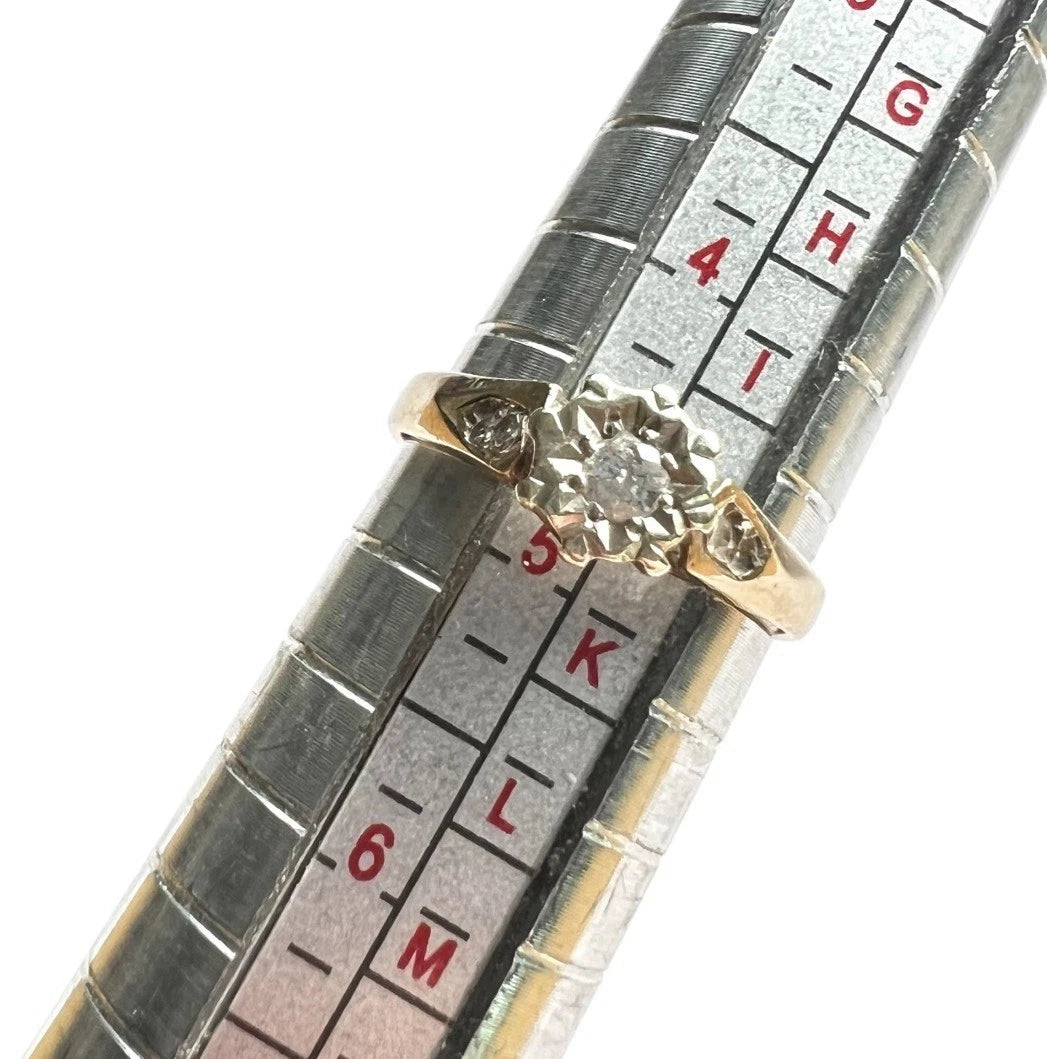 Gold ring with a diamond next to a ruler for size measurement on a white background