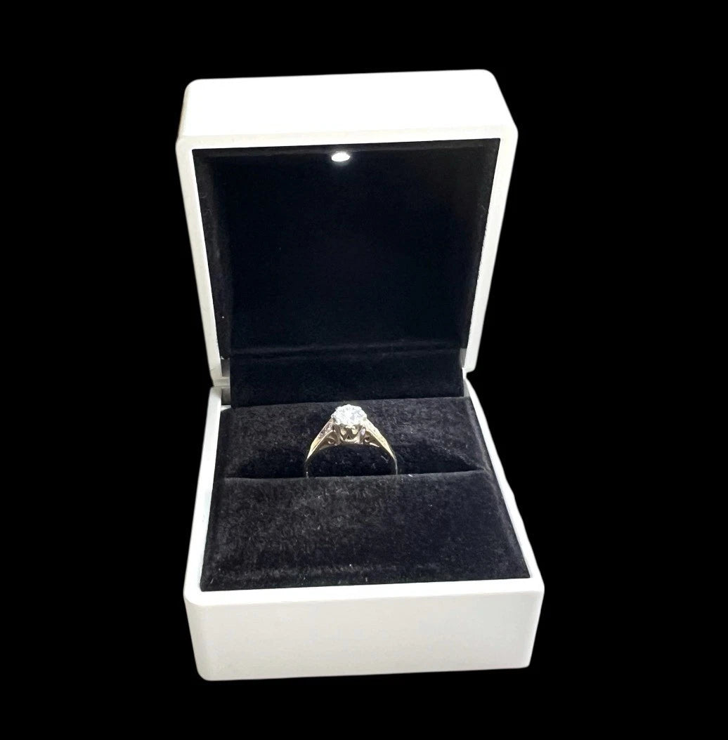 Gold diamond solitaire ring in a white box with a black interior