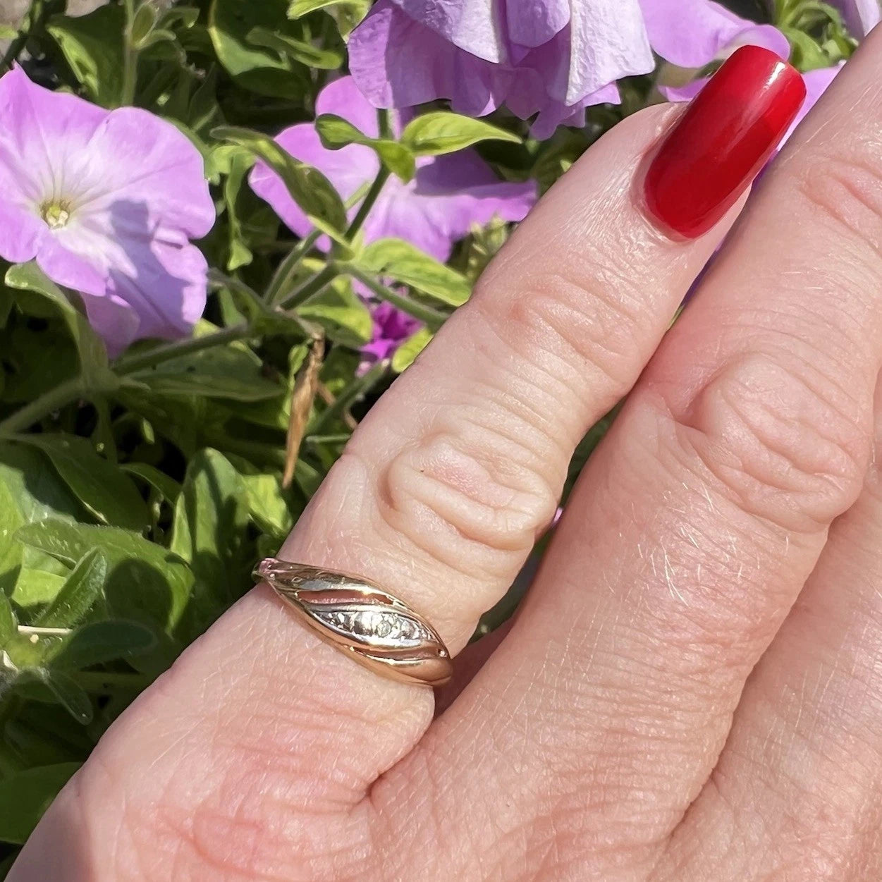 Hand wearing a gold diamond twist ring with pink flowers in the background