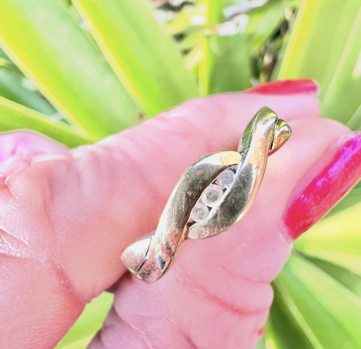 Gold ring being held by fingers with red nail varnish on a green leafy background