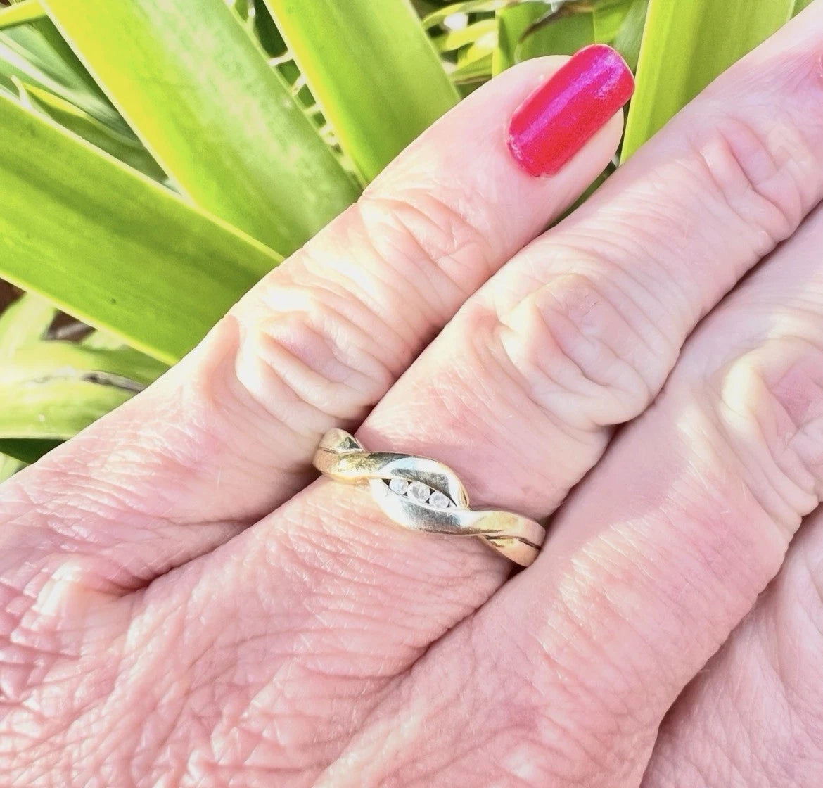 Hand wearing a gold three stone diamond ring with green leaves in the background