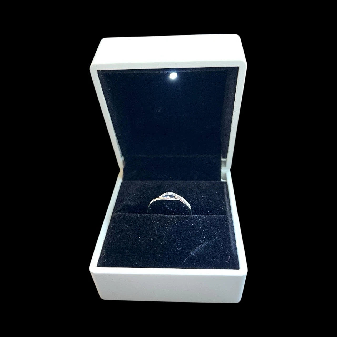 Open jewellery box with a white gold diamond ring inside on a black background