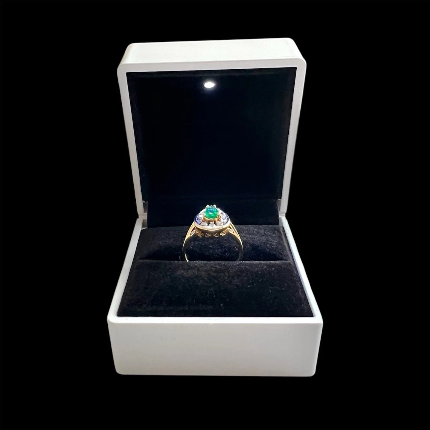 Gold ring with emerald gemstone and diamond halo in a white box on a black background