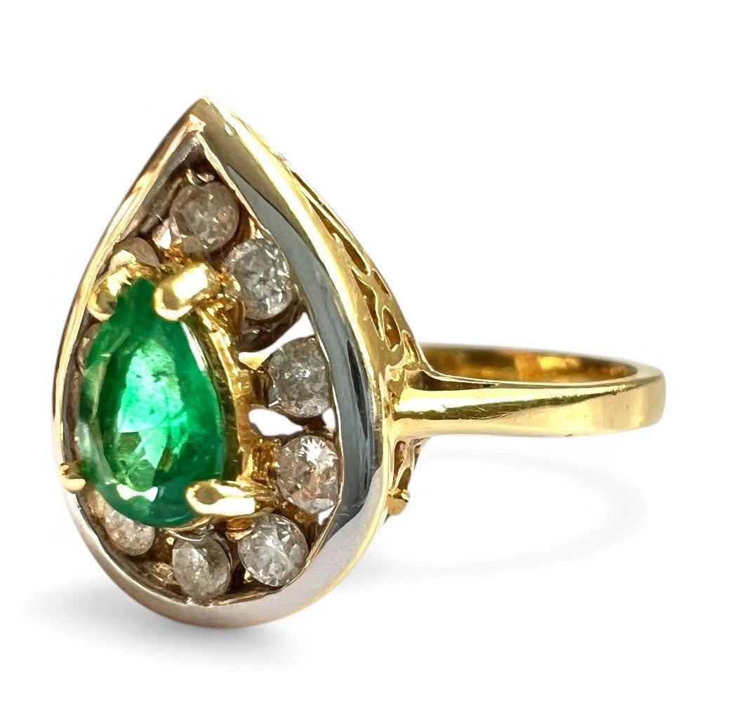 Gold ring with a green emerald gemstone and smaller diamond halo on a white background