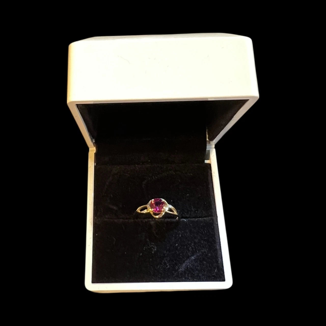 Gold ring with a red garnet gemstone in a white jewellery box on a black background