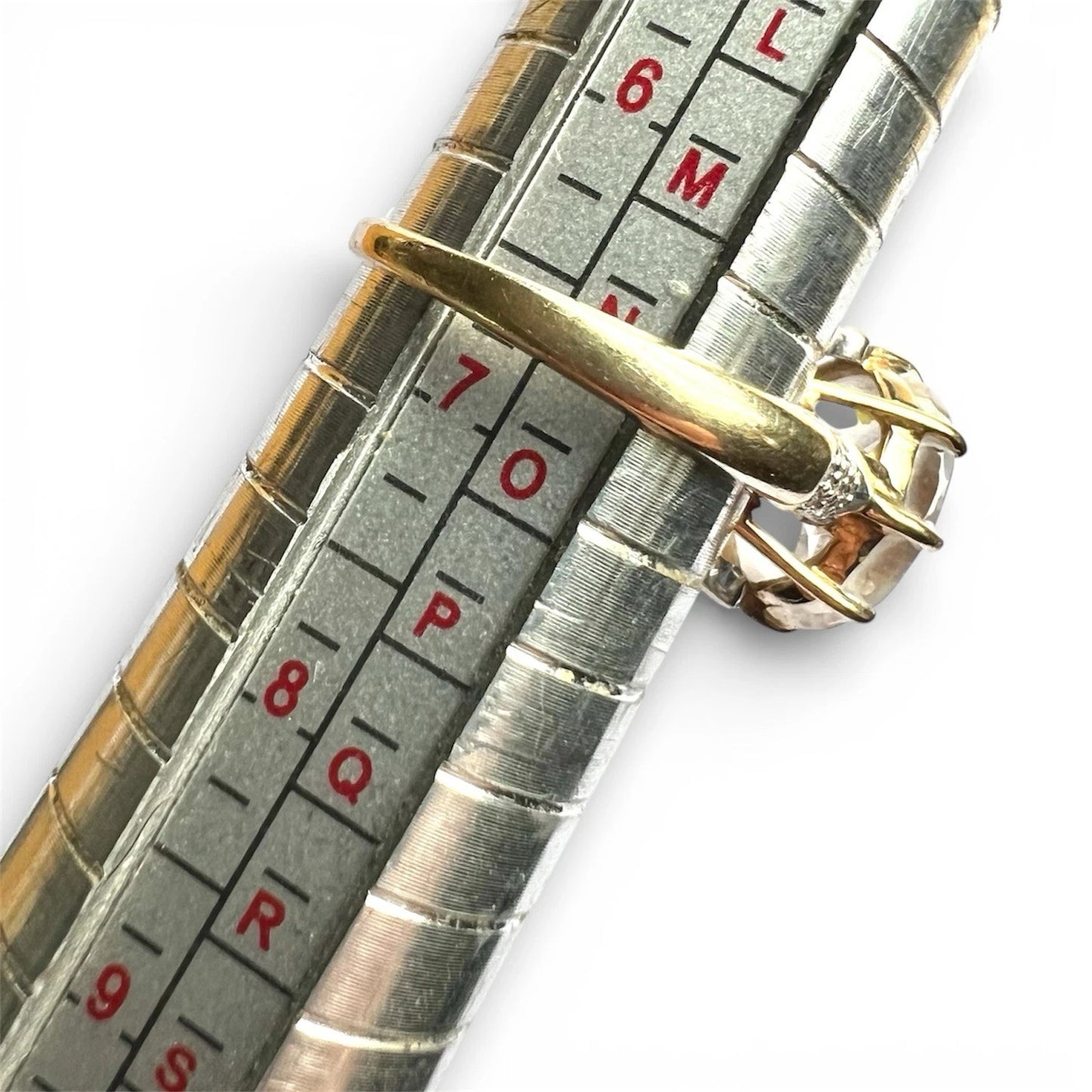 Gold ring on a silver ring size guide with measurement markings.