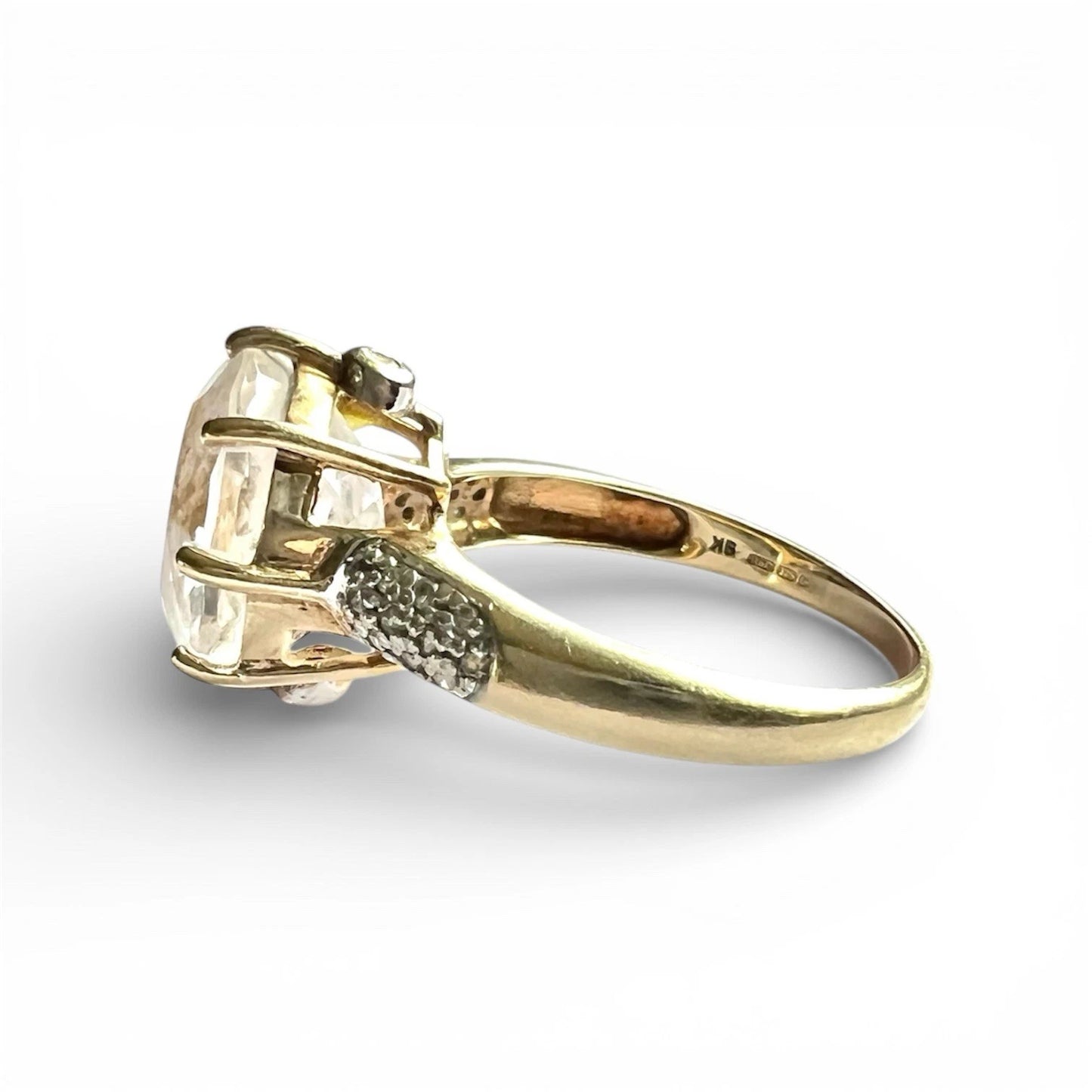 Gold ring with a large quartz gemstone and smaller stones on a white background close up side view 