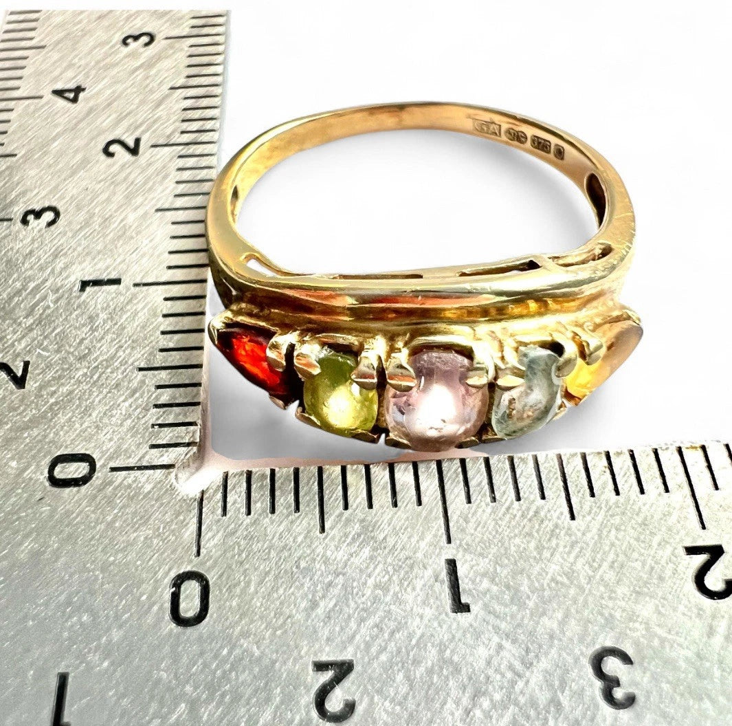 Gold ring with colorful gemstones next to a ruler for size reference