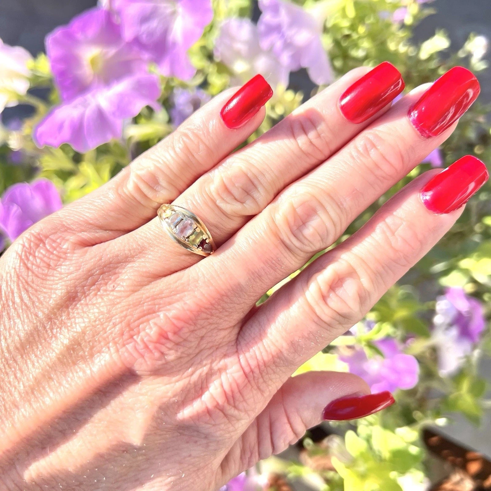 Hand with red nails and a ring against a blurred floral background
