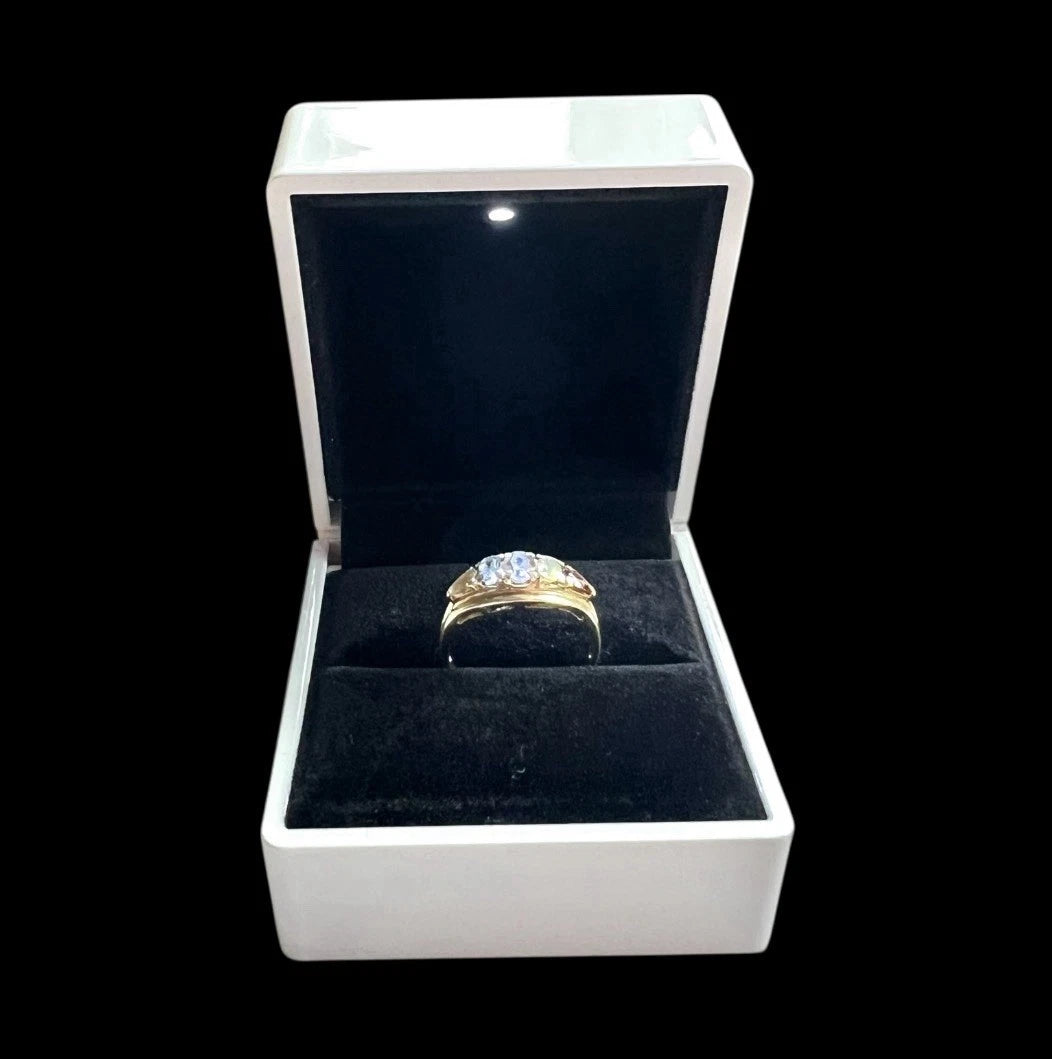 Gold ring with multicoloured gemstones in a white box on a black background