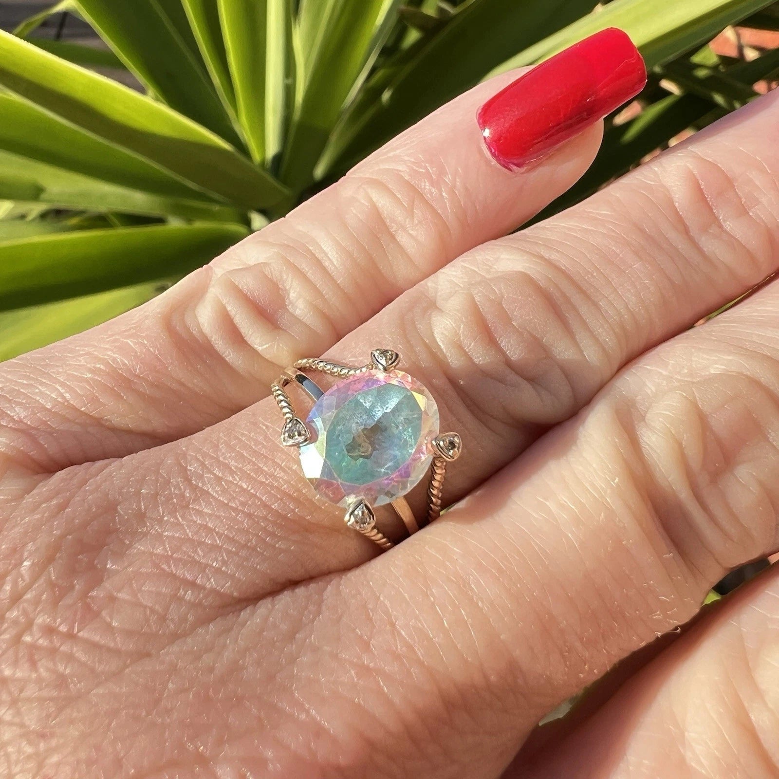 Hand wearing a ring with a colourful mystic quartz gemstone against a plant background