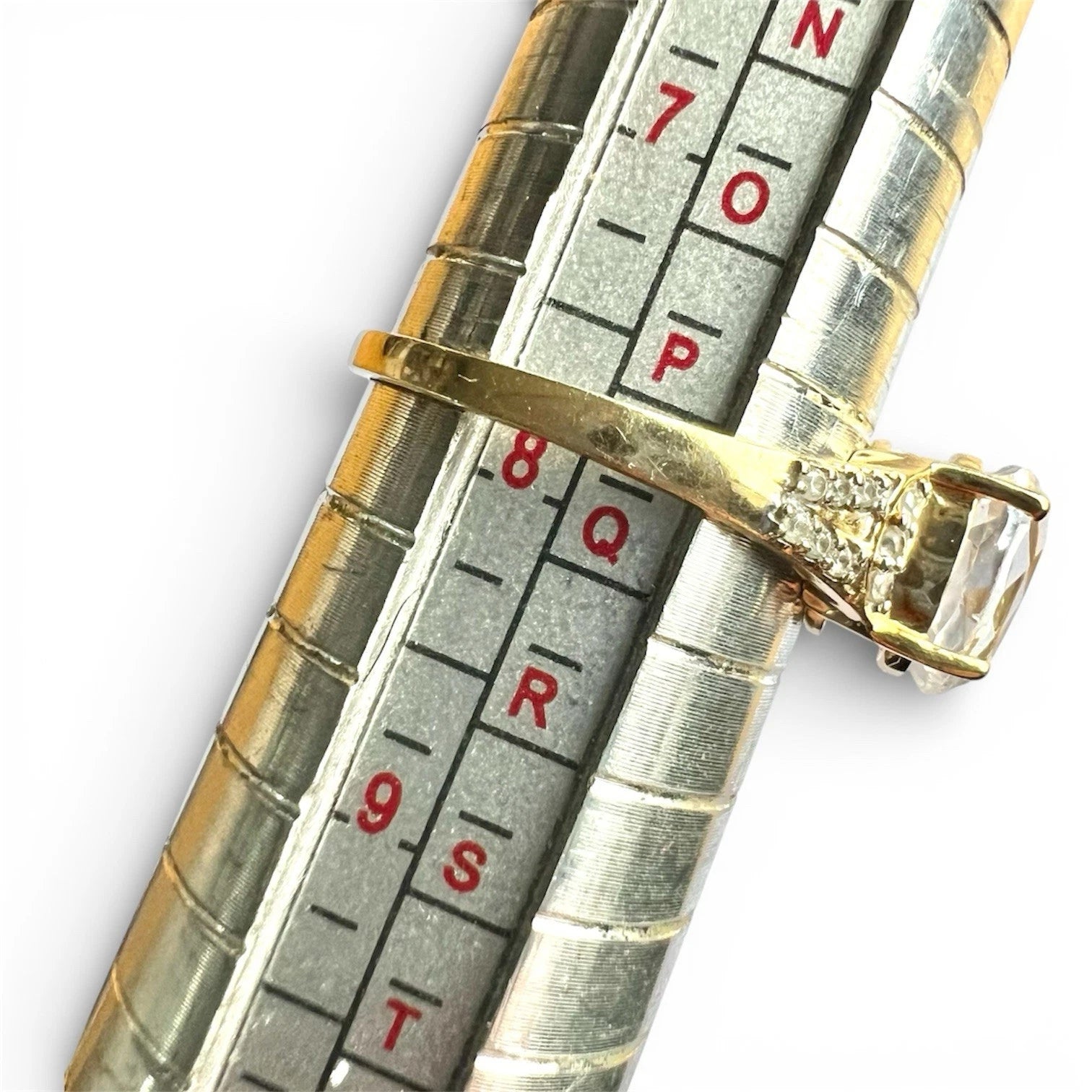 Close-up of a gold ring in a ring sizer gauge with a gemstone on a white background