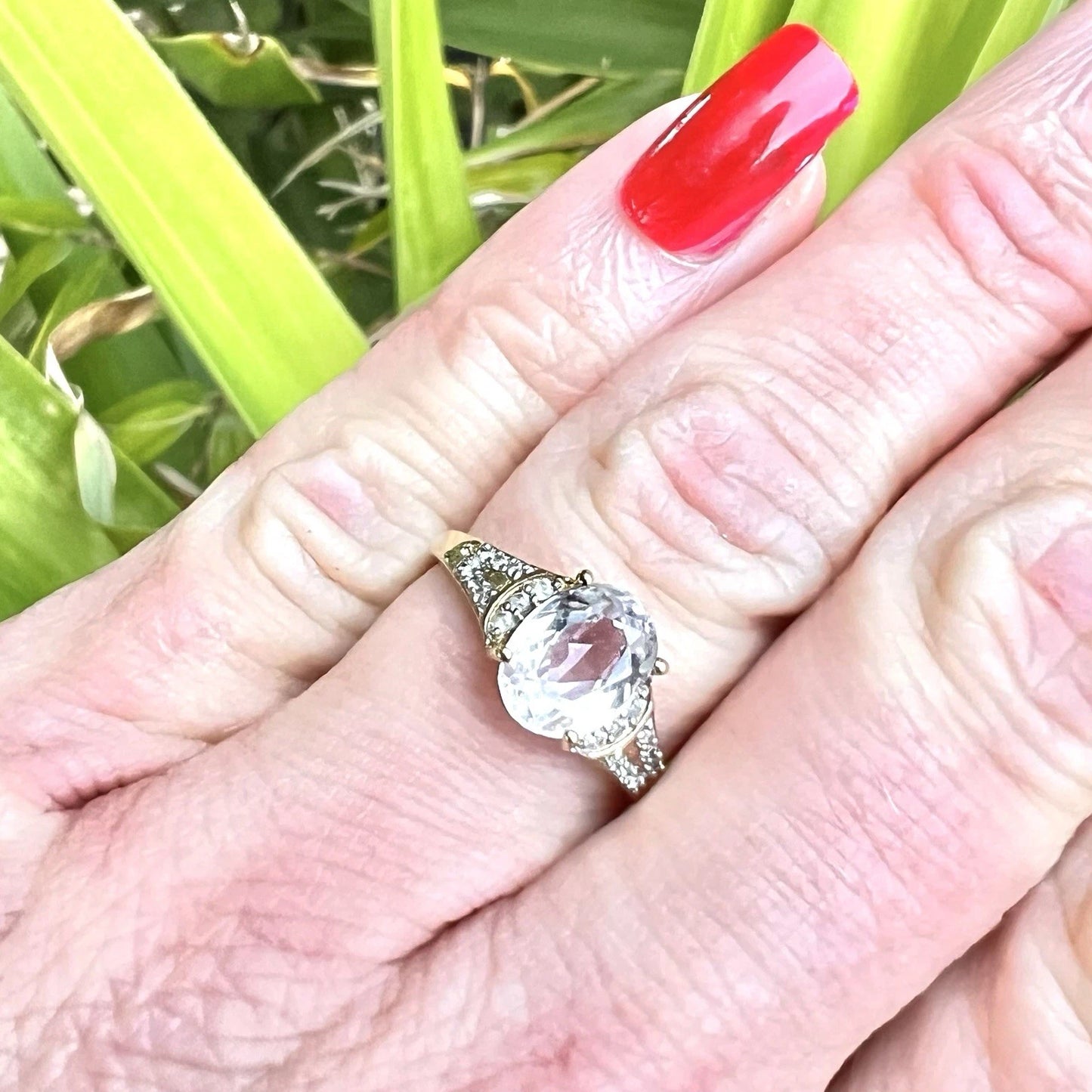 Hand wearing a ring with a quartz gemstone and diamonds against a green background