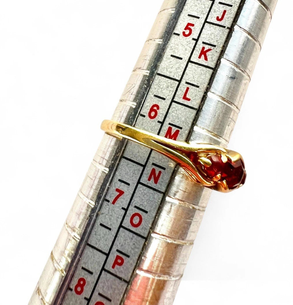 Gold ring with a red gemstone on a metal ruler for size measurement.