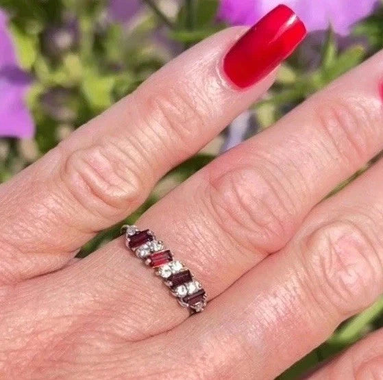 Hand wearing a ring with red gemstones against a blurred floral background