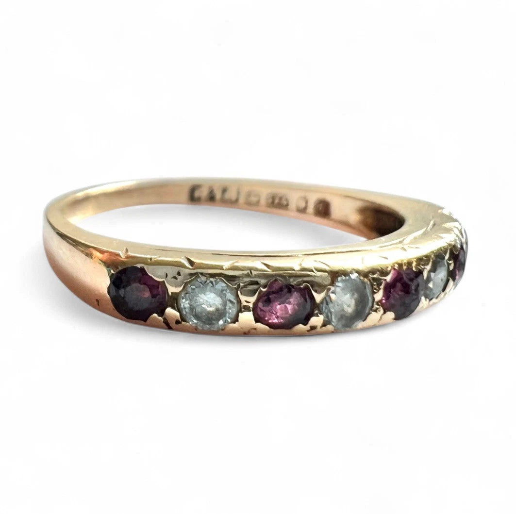 Gold ring with embedded ruby and CZ gemstones on a white background, close up view of setting 