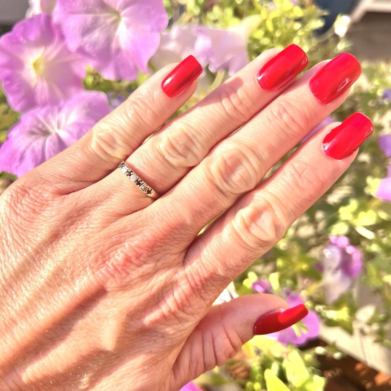 Hand with Ruby and cubic zirconia eternity ring on hand with red nails, set against a blurred floral background