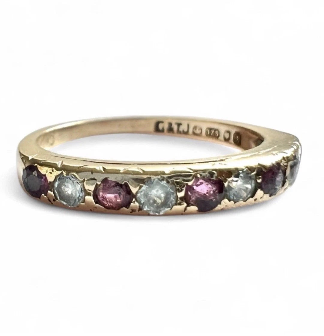 Close up of gold ring with red rubies and cubic zirconia gemstones with visible hallmark on a white background