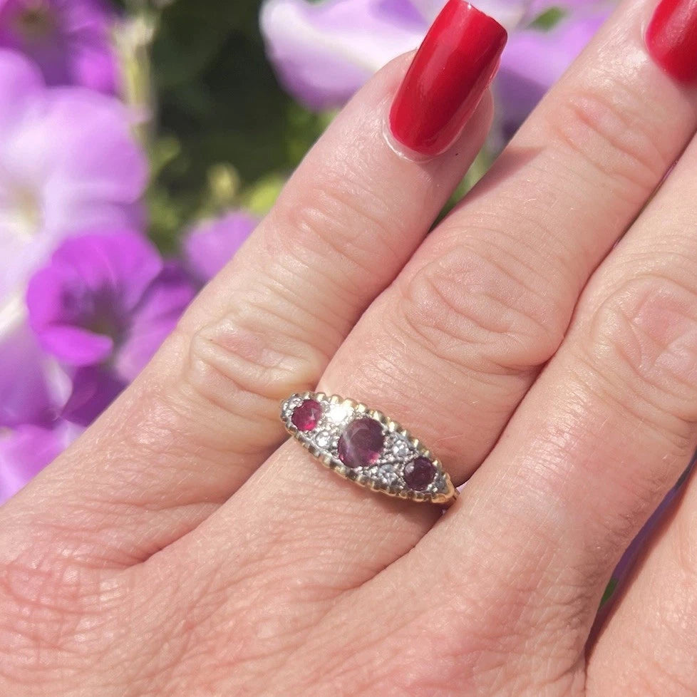 Antique Ring with Ruby and diamond gemstones on a hand against a blurred floral background