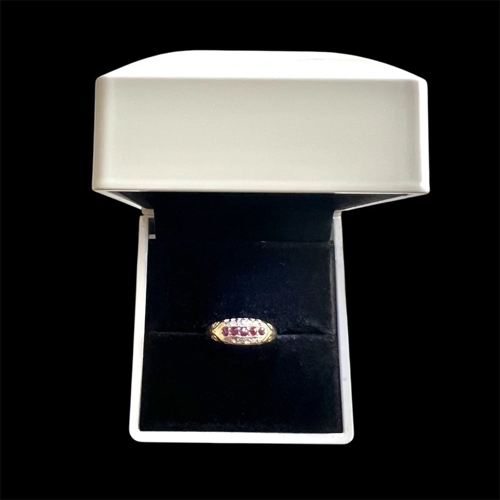Edwardian gold three row ring set with rubies and diamonds on a black cushion in a white jewellery box