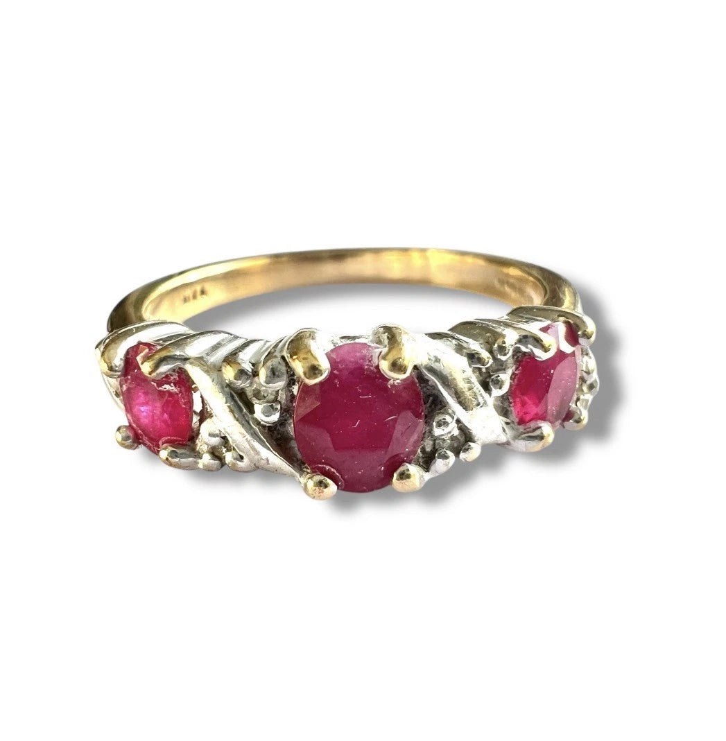 Gold ring with three red ruby gemstones and diamonds on a white background, close up front view of setting and gemstones