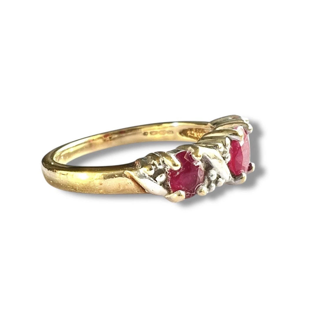 Vintage gold ring with three ruby and diamond's on a white background, close up side view of setting and gold band 