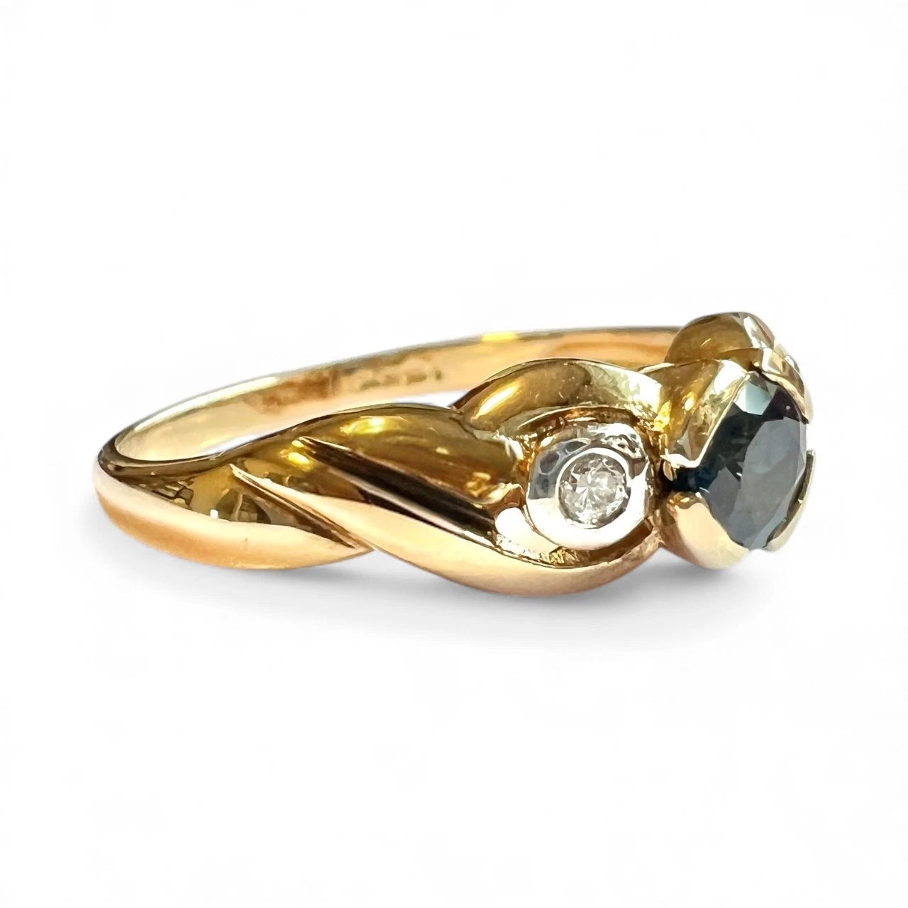Gold ring with blue sapphire gemstone and diamonds on a white background, close-up side view of setting 
