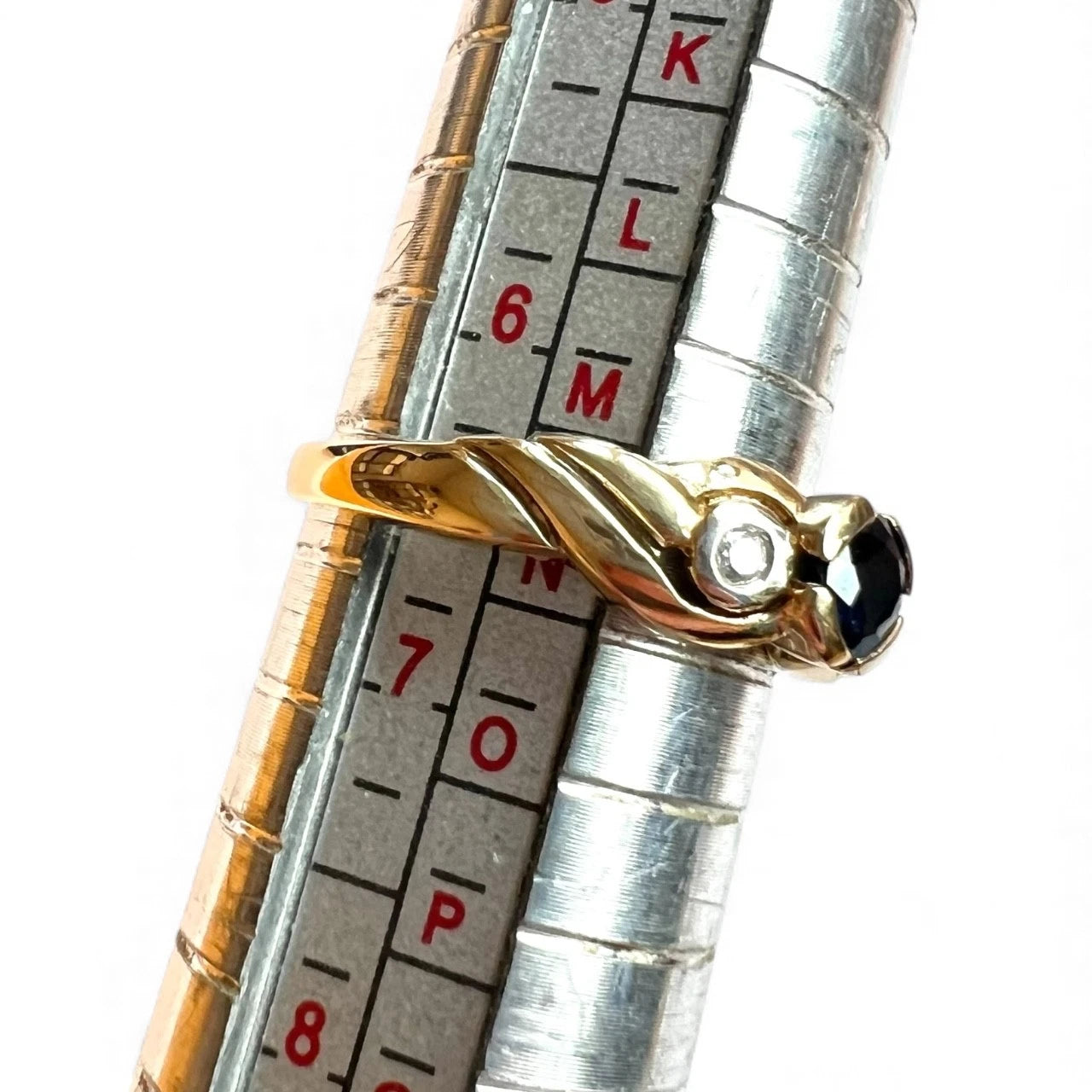 Gold ring with a diamond on a silver ruler with measurement markings.