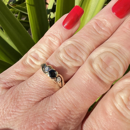 Close-up of a hand wearing a gold ring with blue sapphire gemstone against a green leafy background