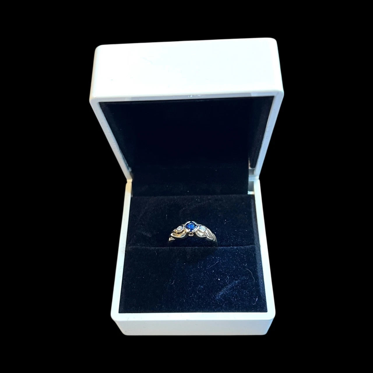 Gold ring with blue and diamond in an open jewellery box on a black background