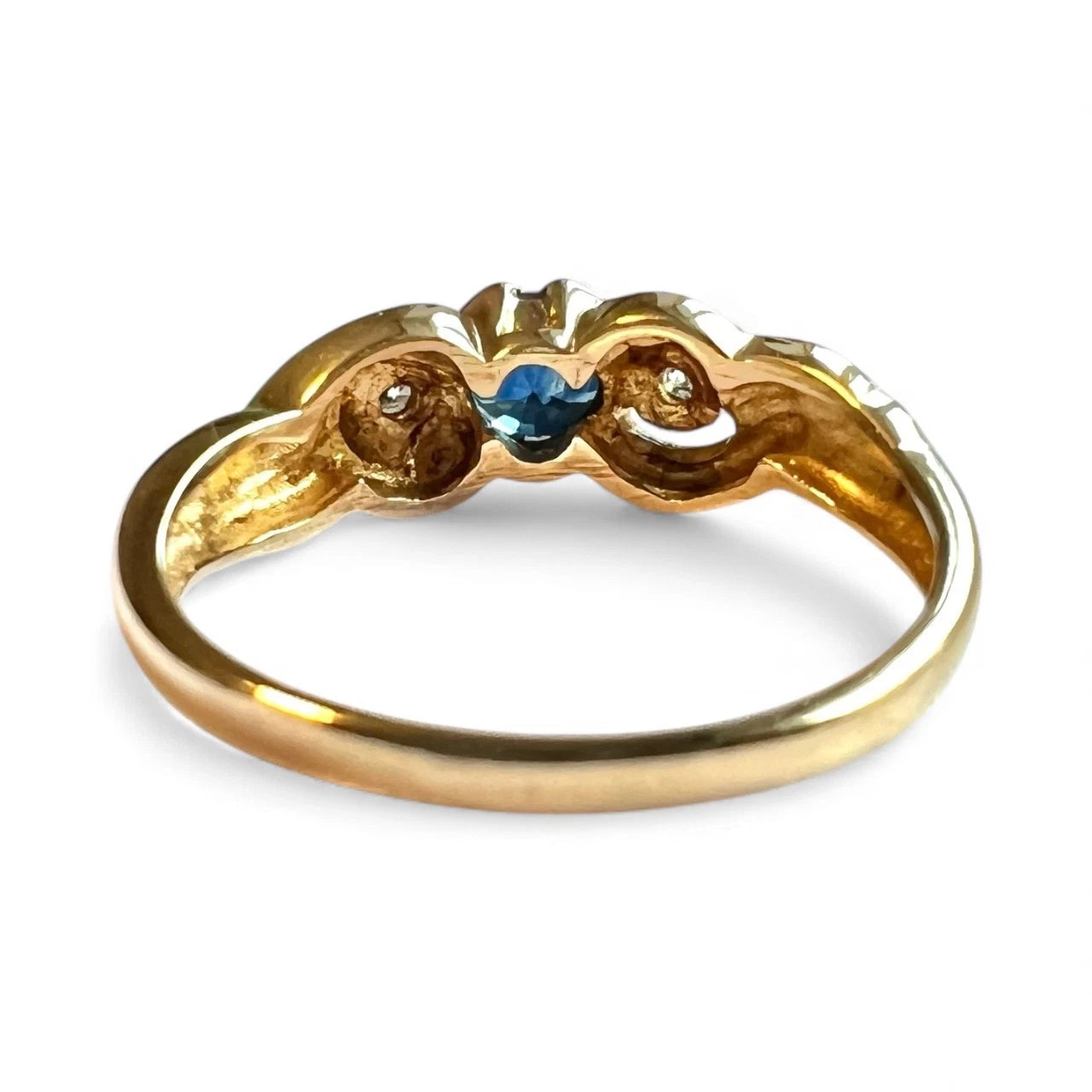 Gold ring with a blue sapphire and diamond on a white background, close up rear view of setting and gold band 