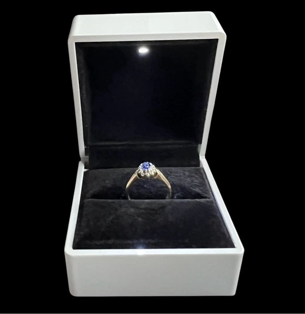 Gold ring with a blue sapphire gemstone and diamonds in an open jewellery box on a white background