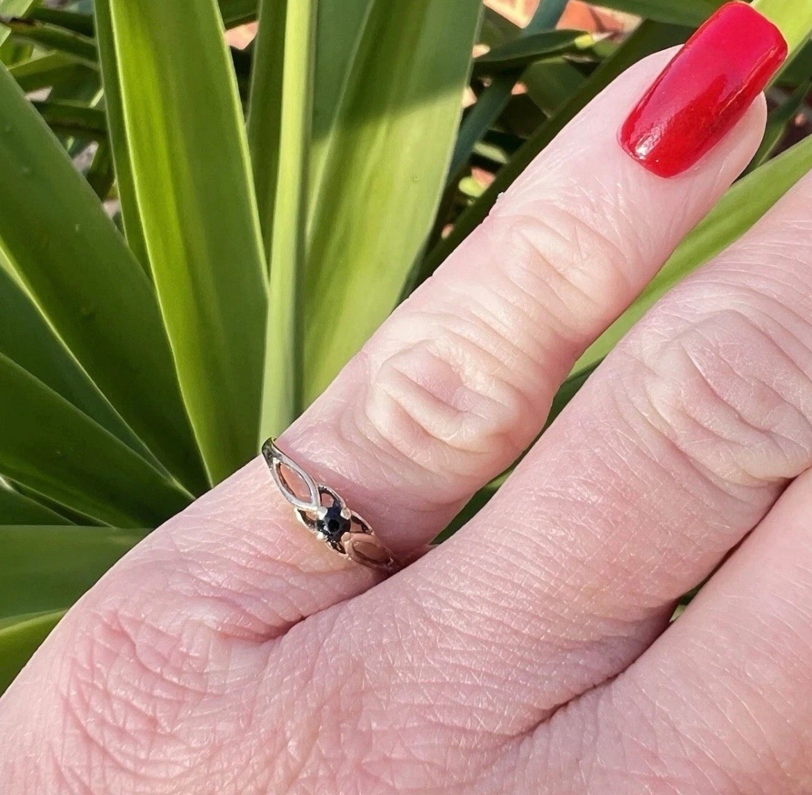 Hand wearing a ring with a blue stone against a green leafy background
