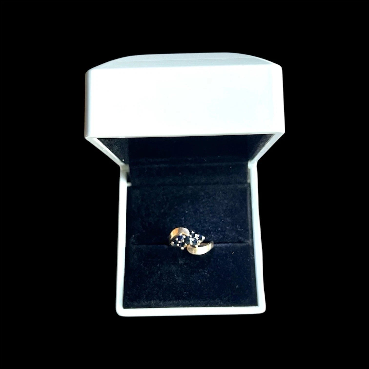 Gold ring with a blue sapphire gemstones in a white box on a black background