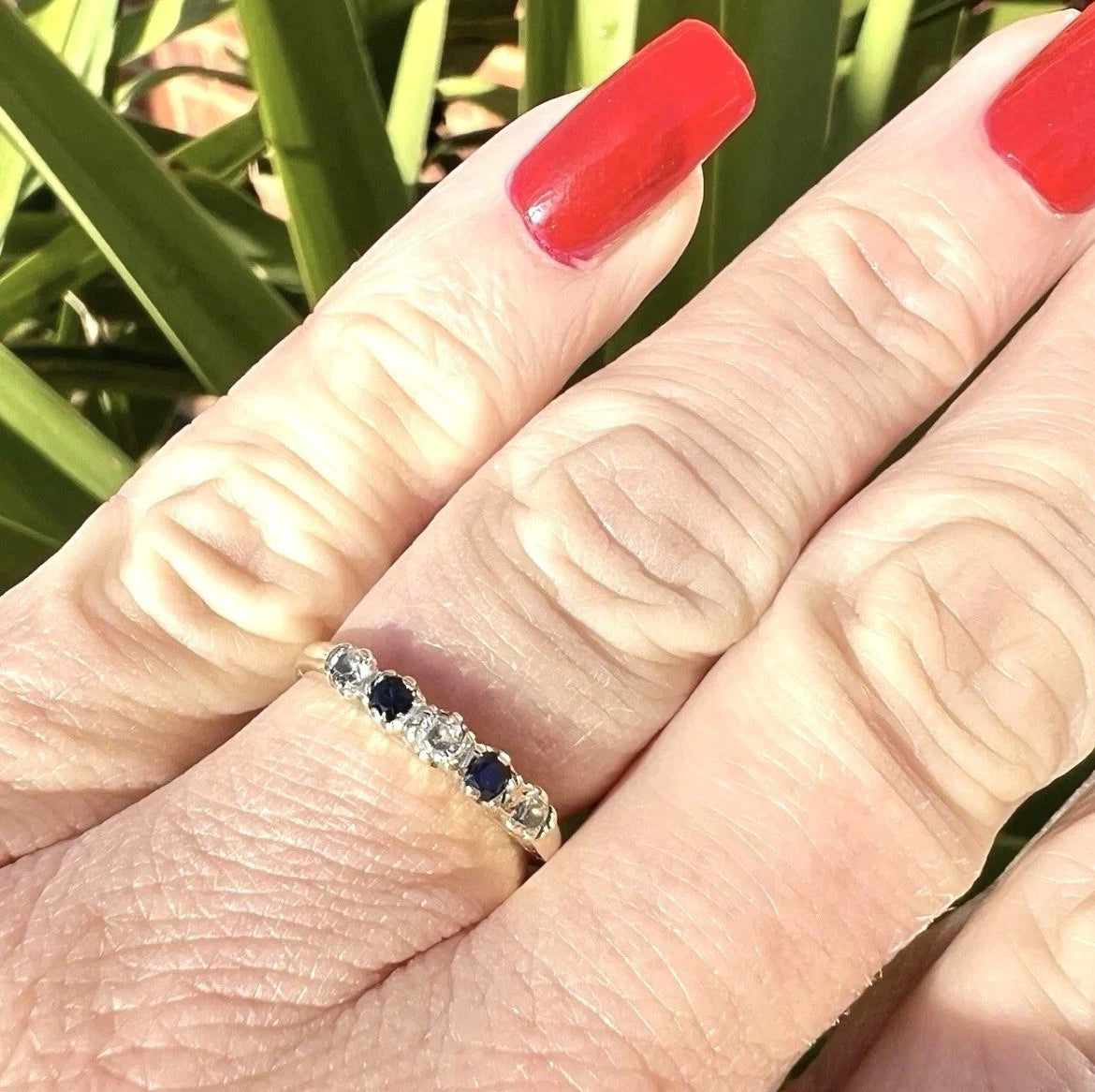 Close-up of a hand wearing a ring with gemstones against a natural background