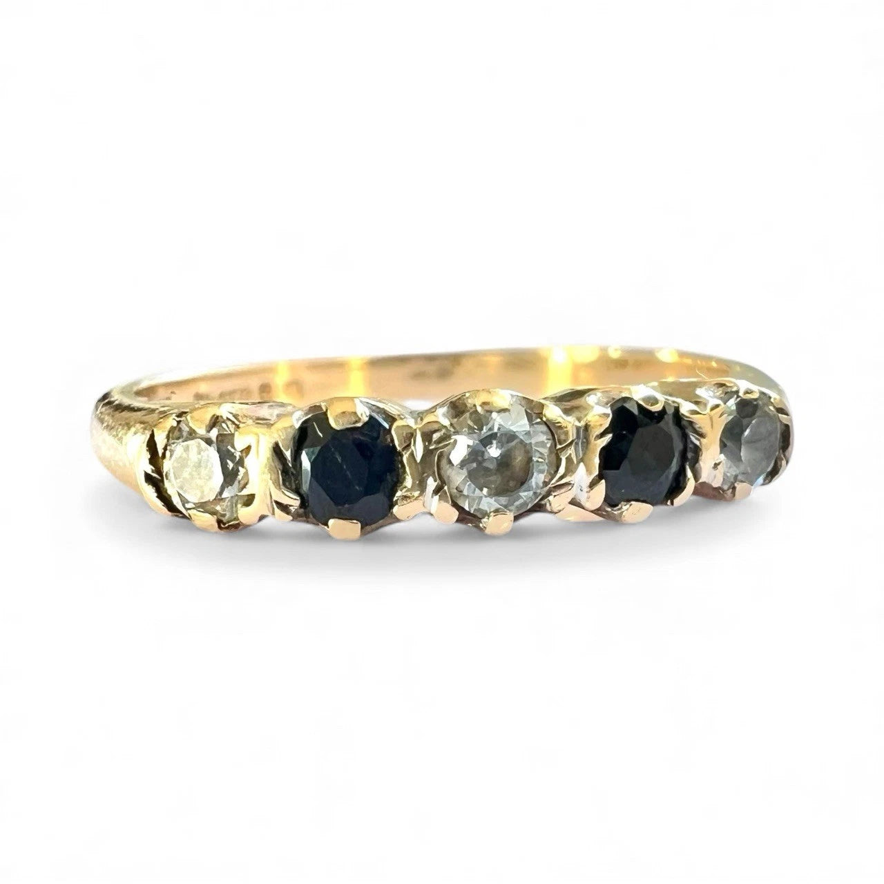 Close up of Gold ring with five alternating sapphire and cubic zirconia gemstones on a white background