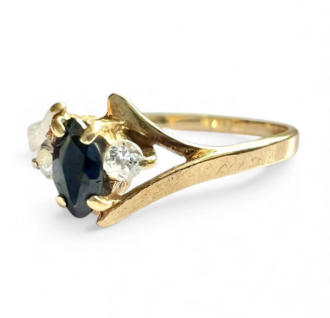 Gold ring with a central sapphire gemstone and two smaller clear stones on a white background