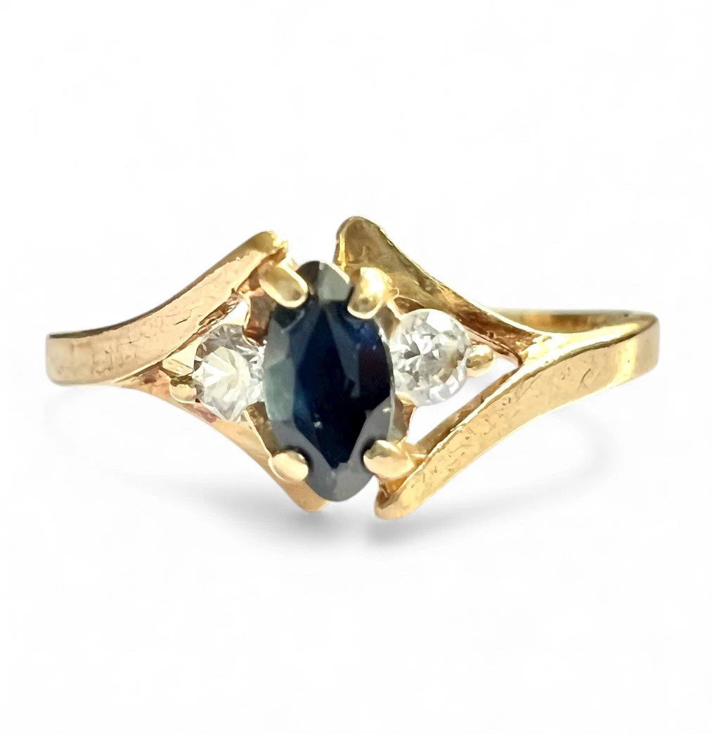 Gold ring with a central blue sapphire gemstone and two smaller clear gemstones on a white background