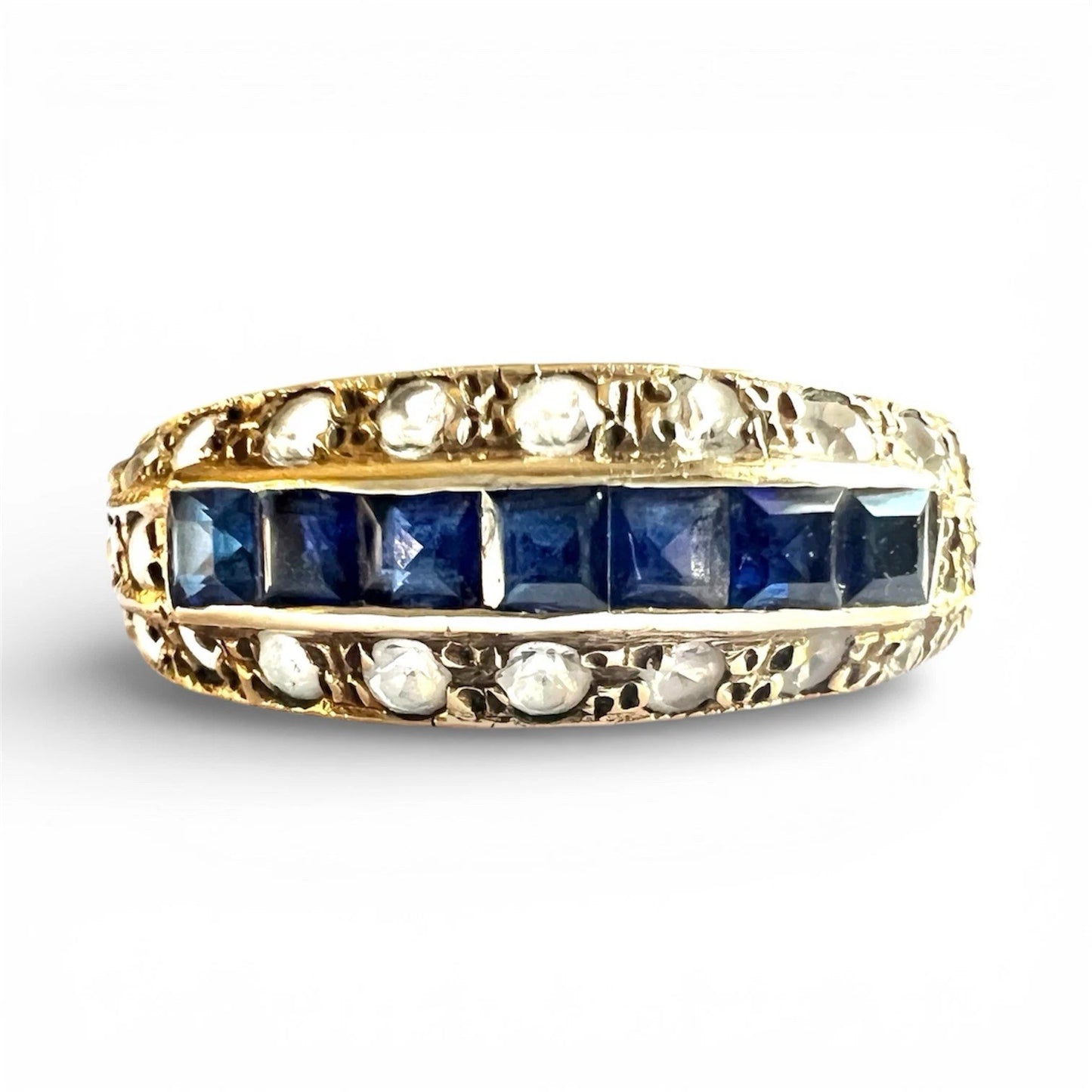 Gold ring with a row of square blue cut sapphires and cubic zirconia on a white background